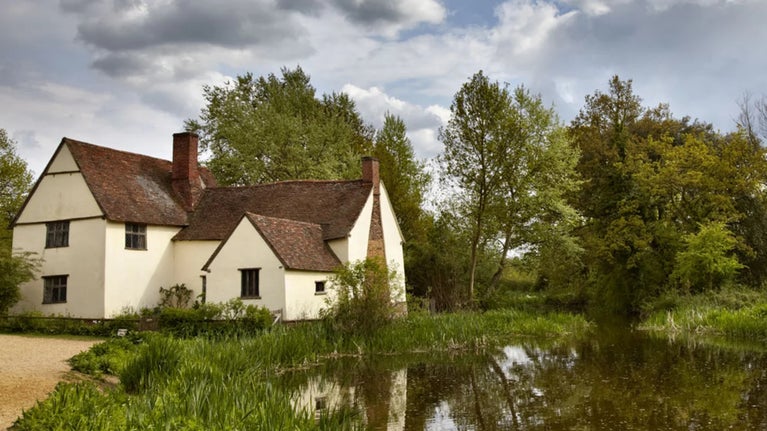 Cream-painted Willy Lott's House stands next to the river Stour at Flatford, Suffolk, reflecting in the water along with mature trees